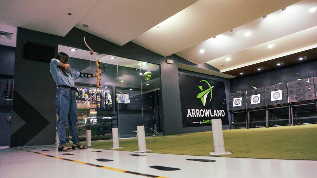 Archer shooting at targets inside Arrowland range with green turf flooring