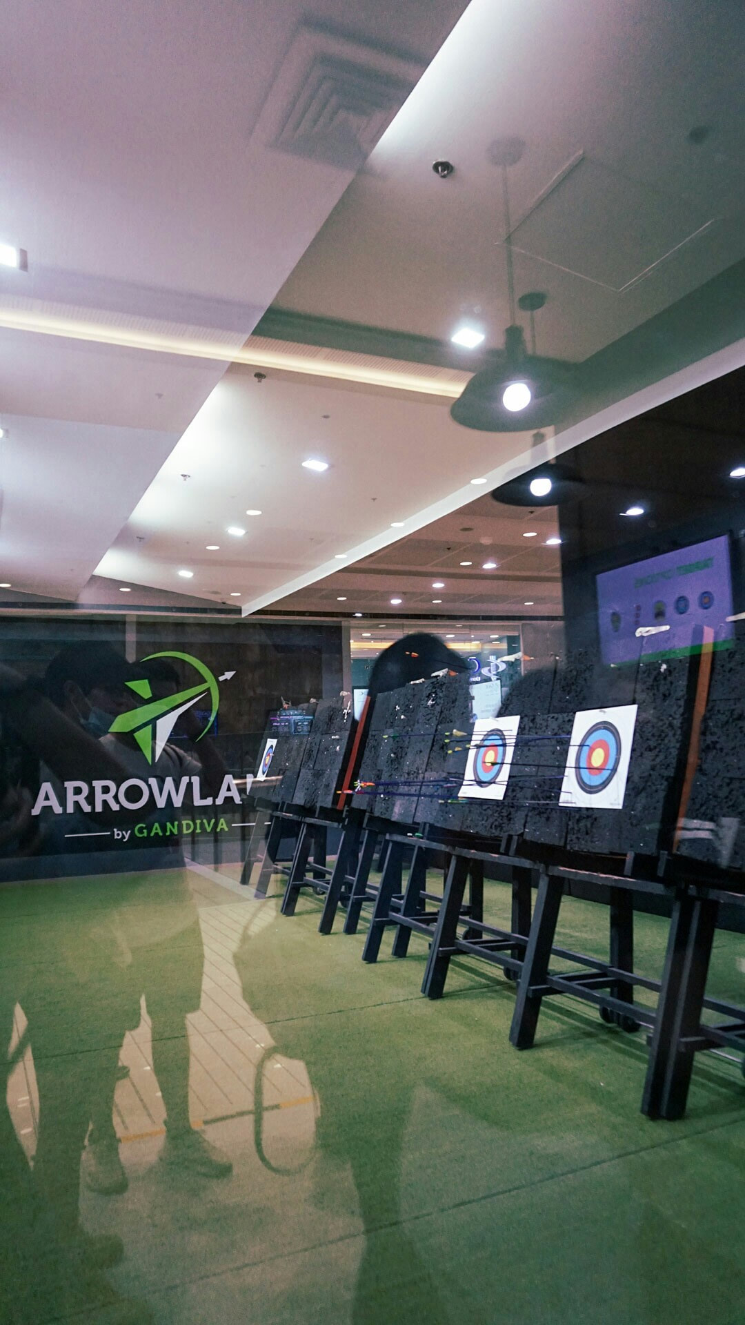 Interior view of Arrowland by Gandiva archery range through glass with logo and targets visible